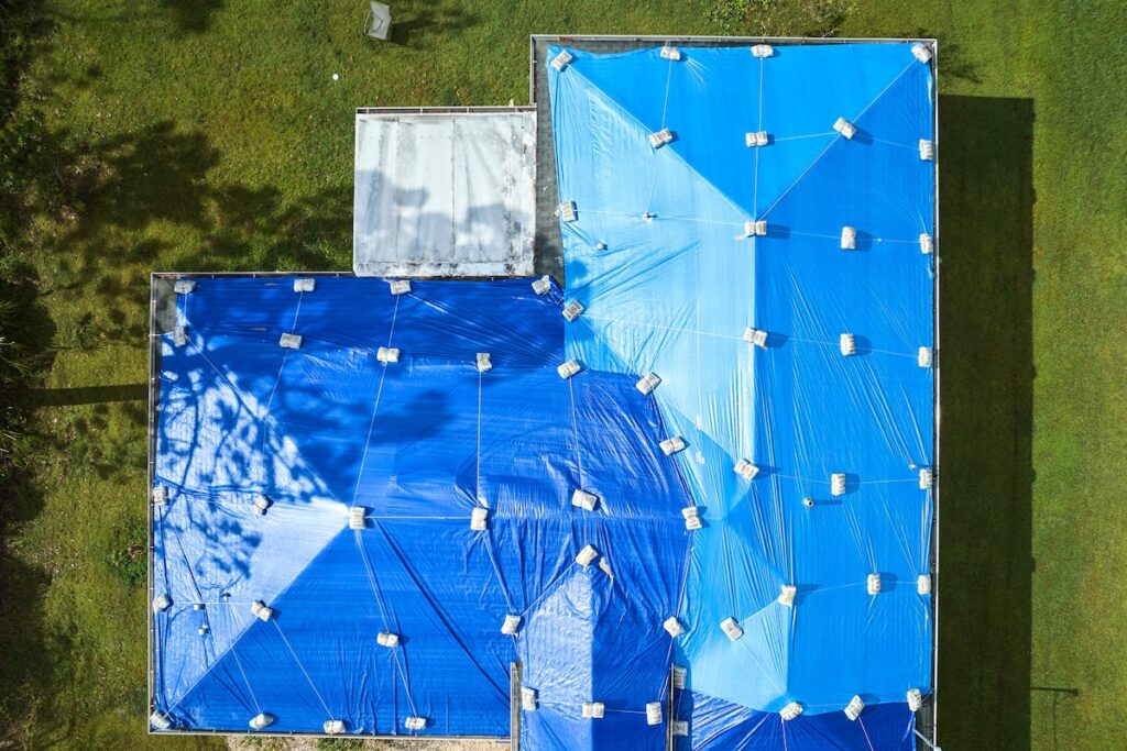Top view of leaking house roof covered with protective tarp sheets against rain water leaks until replacement of asphalt shingles. Damage of building rooftop as aftermath of hurricane Ian in Florida.