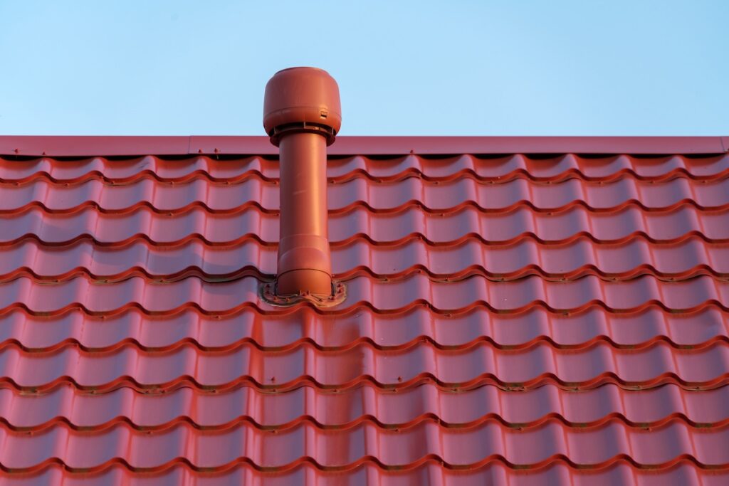 Pipe of a modern ventilation system on the roof of the house with red metal tiles