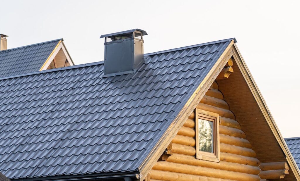 A log cabin features a sleek metal shingle roof and chimney, showcasing a blend of rustic charm and contemporary design in natural light