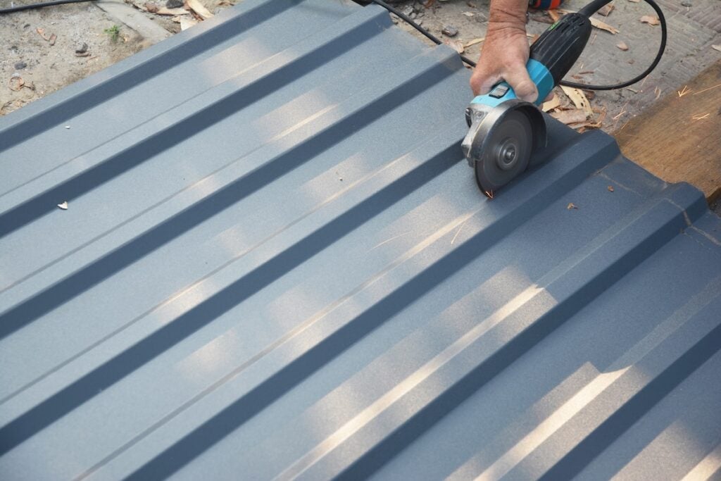 A roofer is cutting with a power angle grinder a corrugated metal roofing sheet, a metal roof tile.