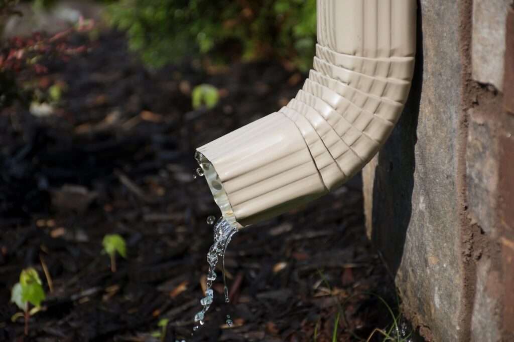 A rain gutter downspout with water coming out