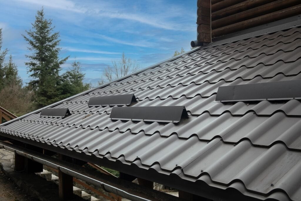 Closeup roof with metal grey shingle tiling surface with rain gutter pipe and snow guard protective fence
