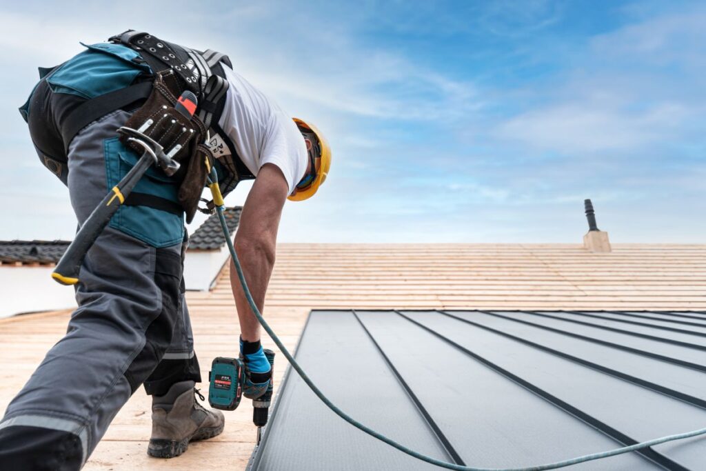 metal roof installation worker using gun on metallic sheet