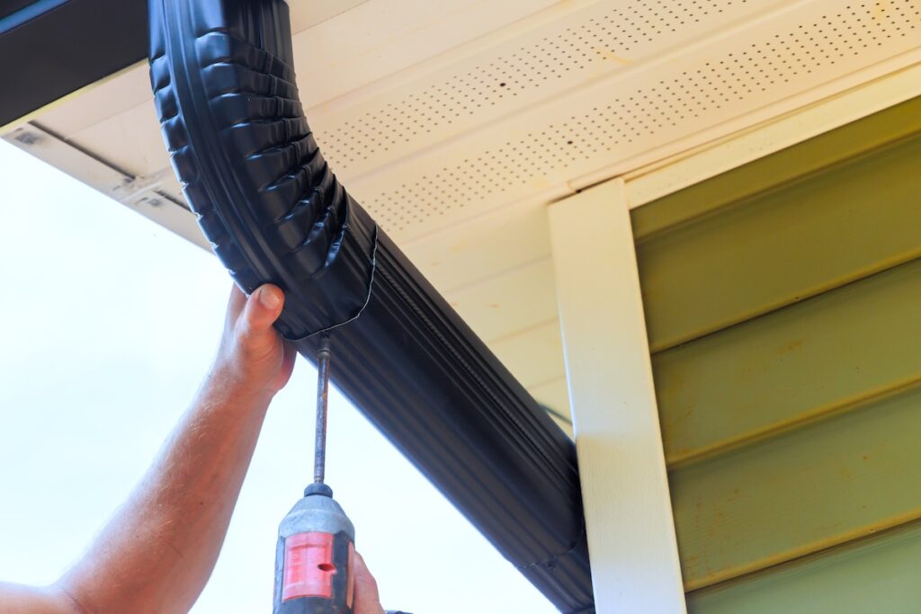 During installation of rain gutters on roofs, worker is fitting downpipe bending downspout