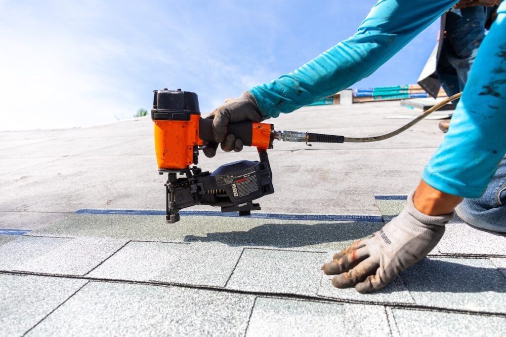 roofer installing roof shingles with pnuematic roofing gun
