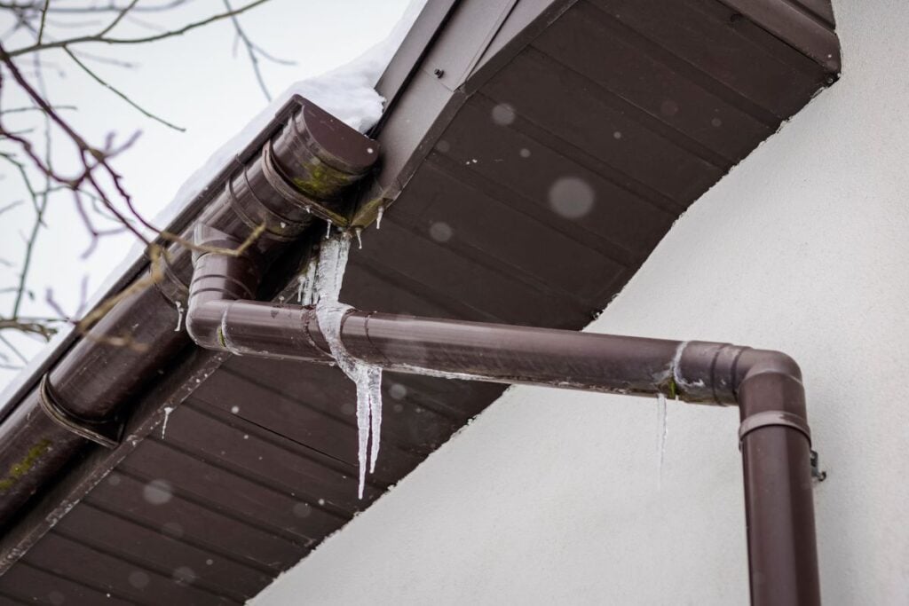 Icicles on Gutter and Snow Drains of House Roof. Ice dams and icicle build-ups on Gutters. Melting Snow on Roof creating ice dam in Gutter.