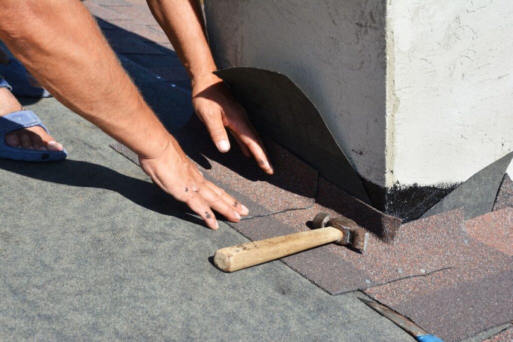 Roofer repair and laying asphalt shingles with vapor barrier in chimney problem area.