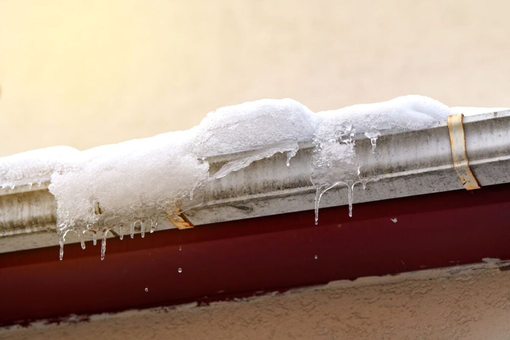 Snow and icicles melting on roof. Risk of snow sliding off building roof. Clogged gutter freeze in winter, ice dams